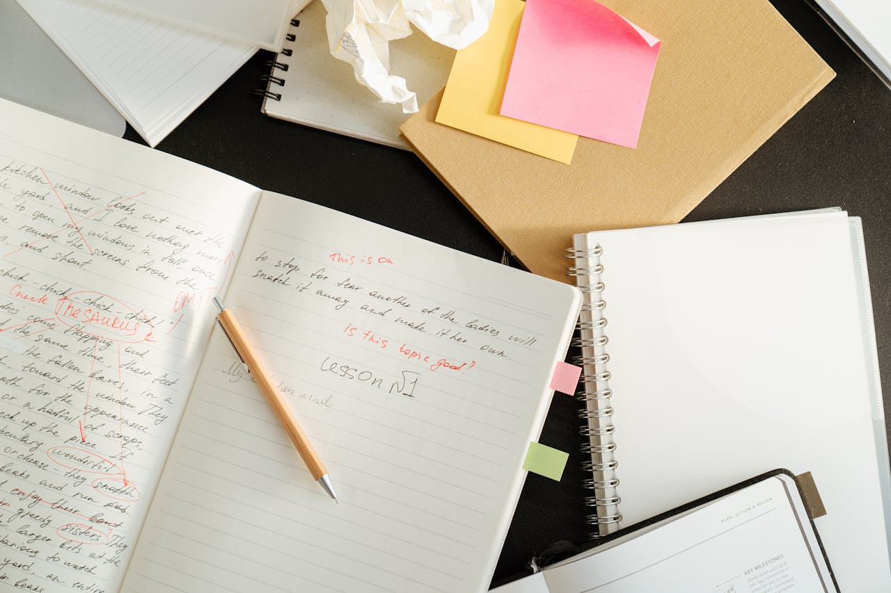 creative-03 A cluttered desk with notebooks, sticky notes, and stationery for educational purposes.