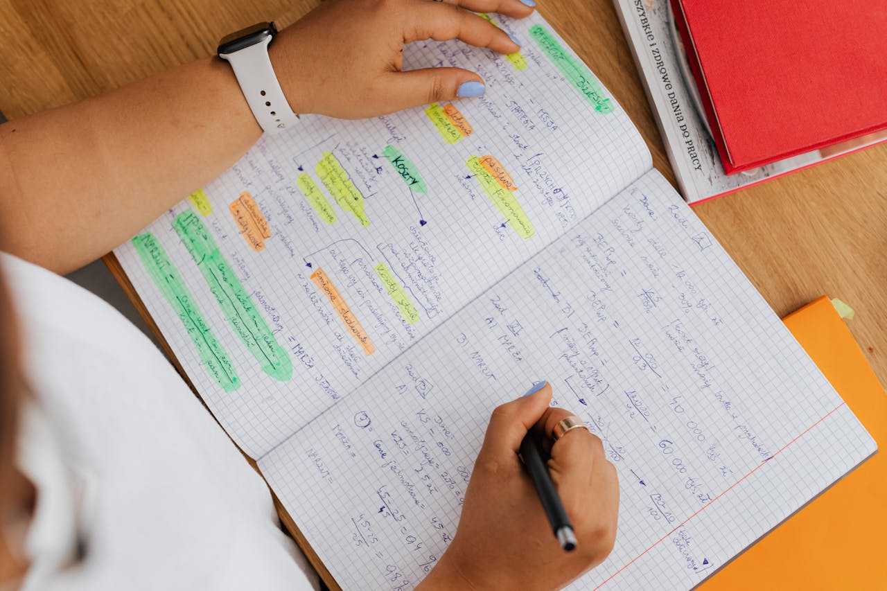 creative-03 Close-up of hands writing in a notebook, highlighting study notes with pens and colorful markers.