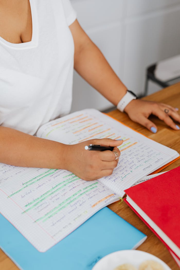 A woman in a white shirt writing with a pen in a notebook. Close-up view.