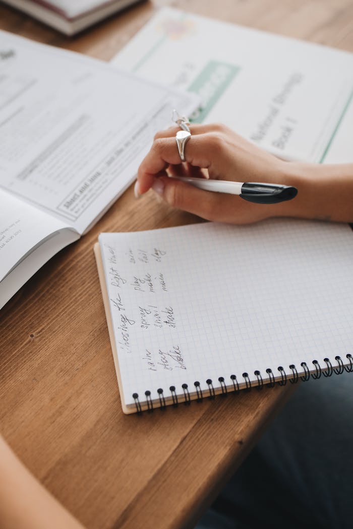 Close-up of hands writing notes in a study environment with open books.
