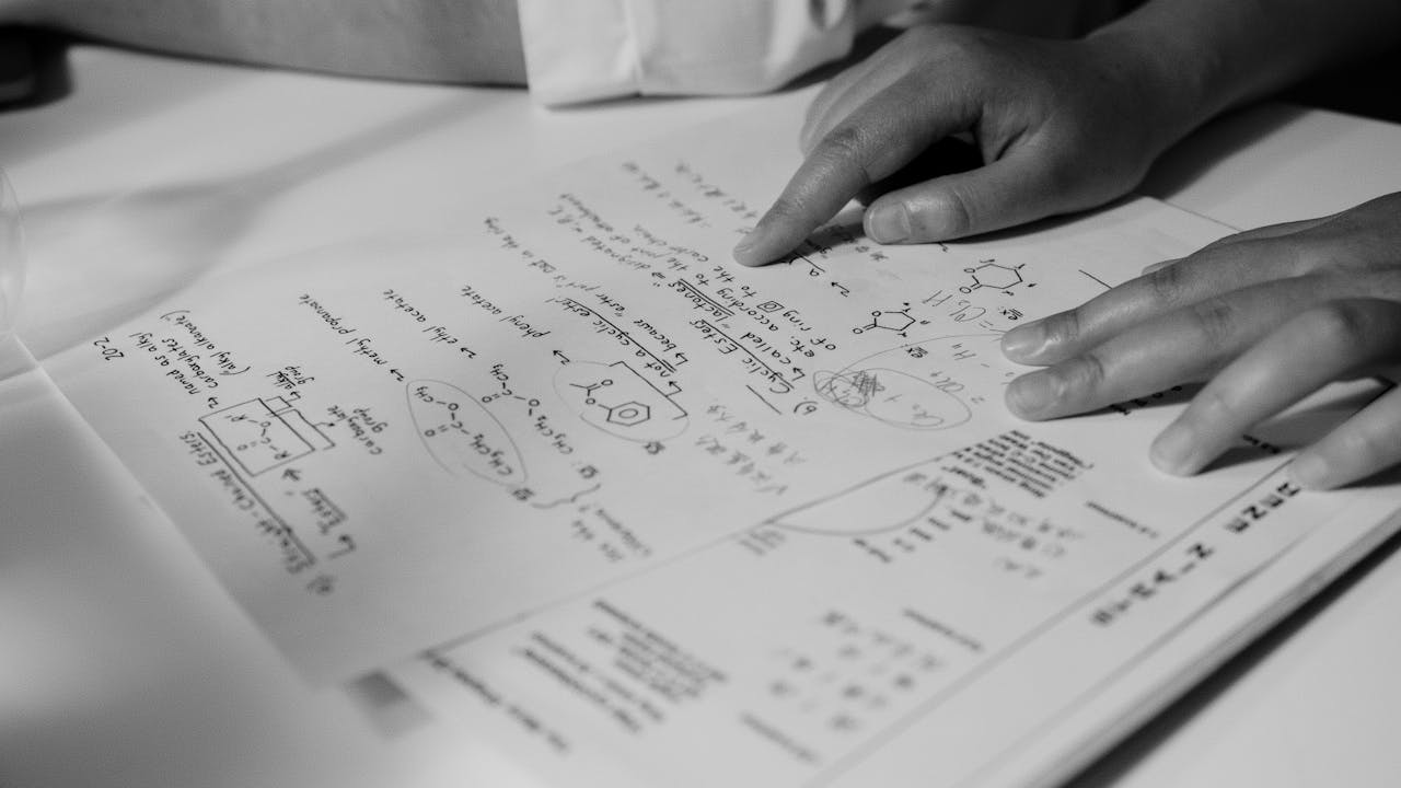 mobile-01 Grayscale photograph of hands pointing at handwritten scientific notes on a paper.